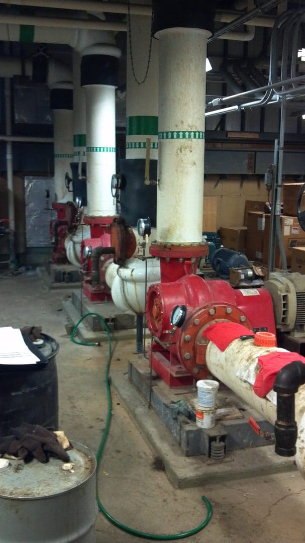 Row of red industrial pumps with large yellow pipes in a factory setting.