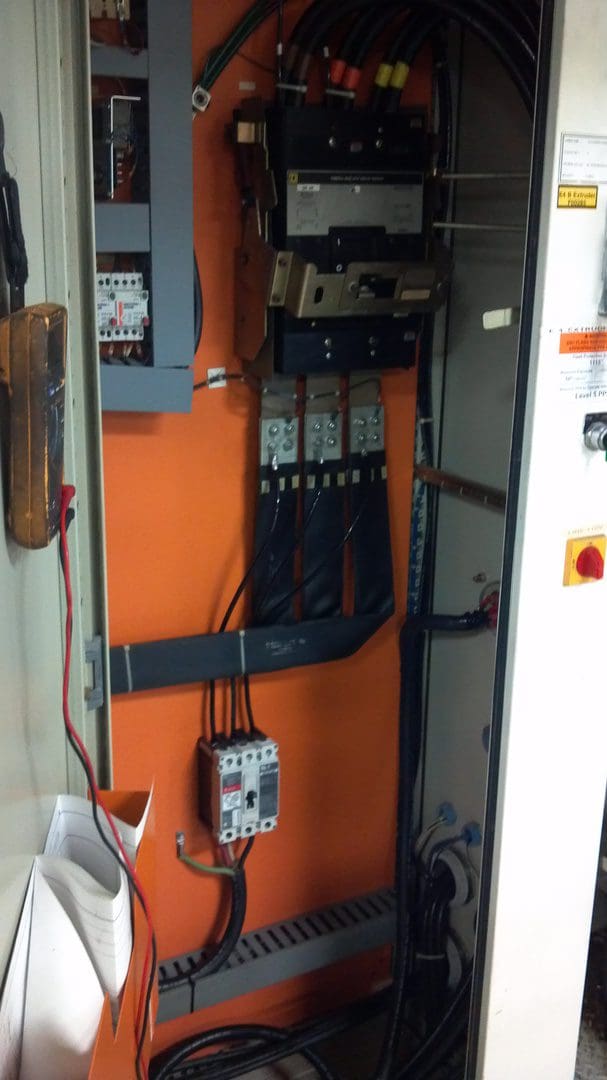 Electrical panel with circuit breakers and wiring inside an orange enclosure.